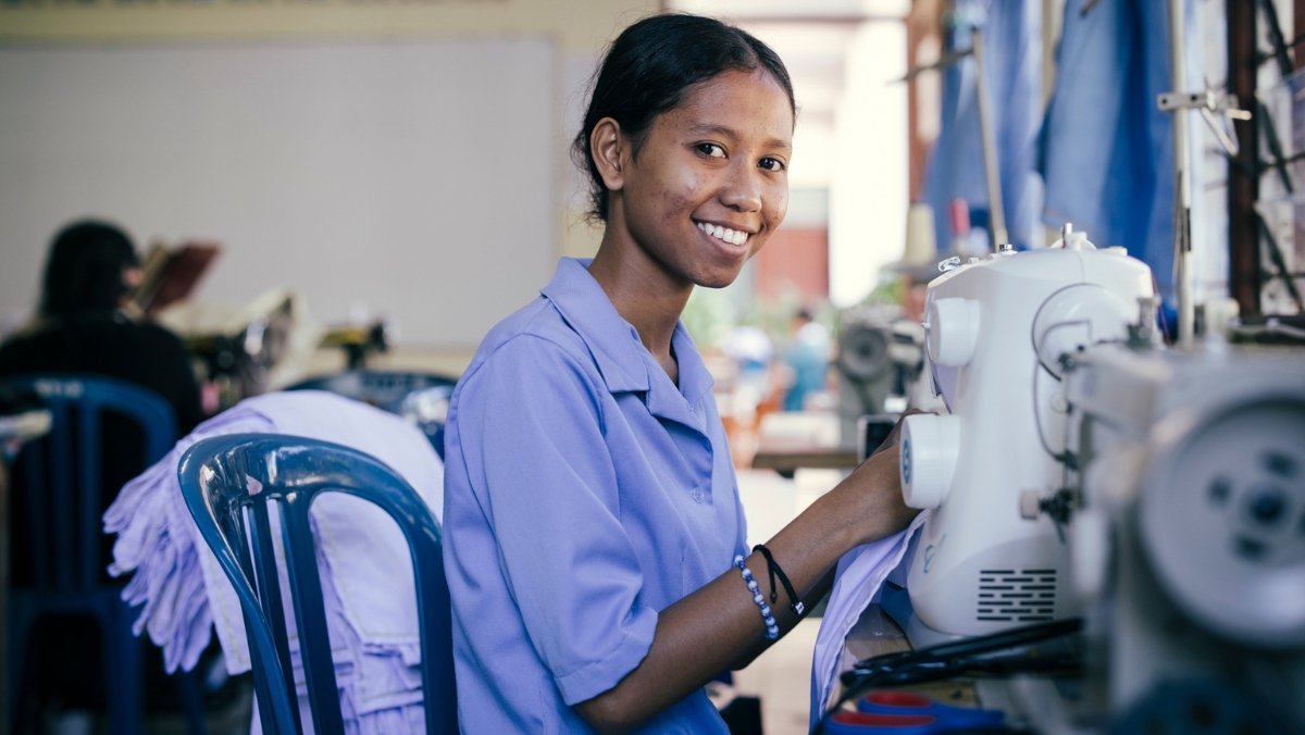 Ein Mädchen sitzt lächelnd vor einer Nähmaschine