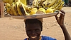 Ein lachender Junge trägt eine Schale mit Früchten auf den Kopf