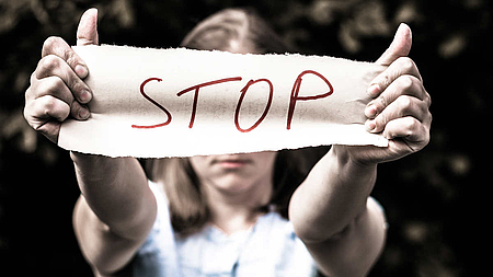 Mädchen hält Banner mit dem Wort "Stop" vor ihr Gesicht