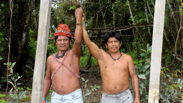 Zwei indigene Männer strecken gemeinsam die Hand nach oben