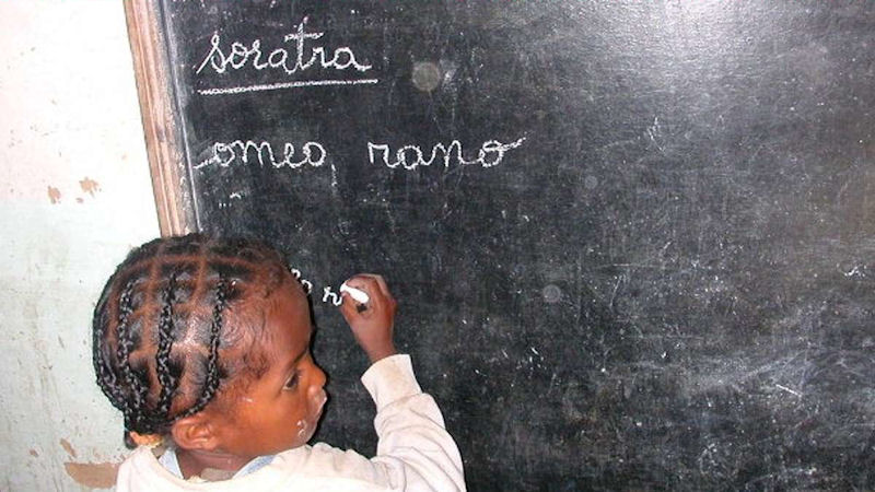 Ein Kind steht an der Tafel und schreibt mit Kreide einige Wörter auf.